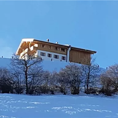 A beautiful house that stands on a snow-covered hill. The sky is clear and blue, with scattered trees in the foreground.