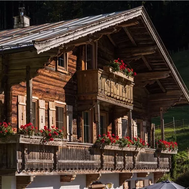 A traditional wooden house with blooming balcony boxes. It is located in a picturesque, green landscape.