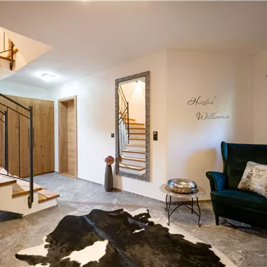 An inviting entrance area with a stylish staircase and a green armchair. A cowhide is on the floor, and a wall bearing the inscription "Welcome" creates a friendly atmosphere.