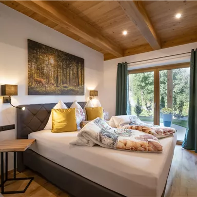 A cozy bedroom with a large bed and soft pillows. The large windows allow for a beautiful view of the garden.