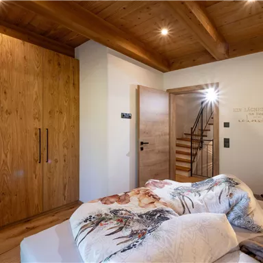 A cozy bedroom with wooden details and a large wardrobe. The stairs lead to another room, while the bedding looks inviting.
