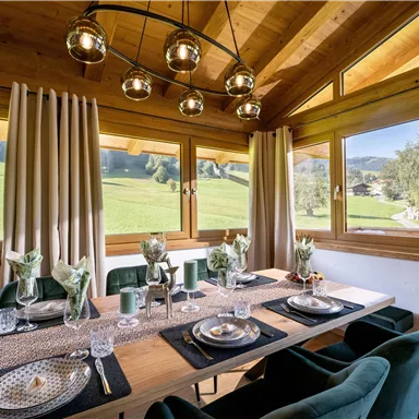 A stylish dining room with a large wooden table and elegant decoration. Large windows provide a beautiful view of the green surroundings.
