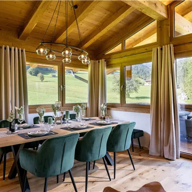 A cozy dining area with a wooden table and green chairs. Large windows provide a beautiful view of the green landscape.