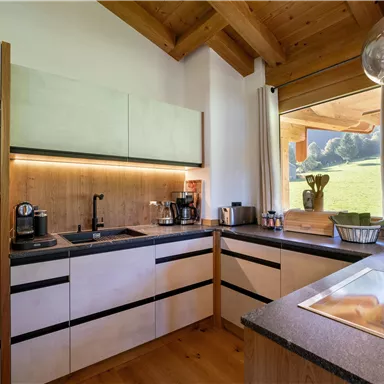 A modern kitchen with wooden shelves and elegant black surfaces. Large window with a view of nature and plenty of daylight.