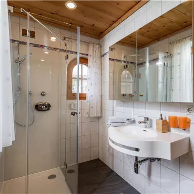 Ein modernes Badezimmer mit einer gläsernen Dusche und einem eleganten Waschbecken. Die Wände sind hell gefliest und es gibt viel natürliches Licht.