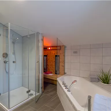 Ein modernes Badezimmer mit einer Duschkabine und einer Badewanne. Die Wände sind hell gefliest und das Licht schafft eine entspannende Atmosphäre.