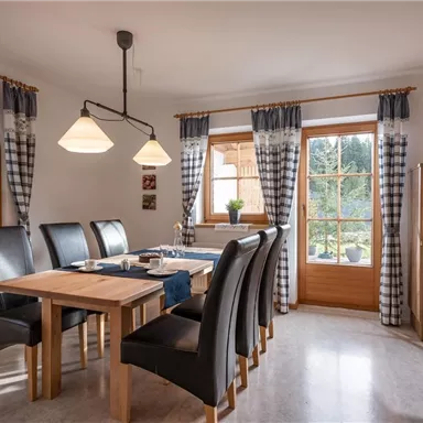 Ein helles Esszimmer mit einem Holztisch und schwarzen Stühlen. Große Fenster bieten Blick auf die Natur draußen.