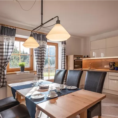 Eine moderne Küche mit einem hellen Esstisch und stilvollen Stühlen. Große Fenster sorgen für viel Tageslicht und eine gemütliche Atmosphäre.