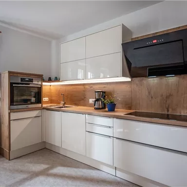 Eine moderne Küche mit weißen Schränken und Holzdetails. Sie enthält einen Backofen, einen Herd und eine Kaffeemaschine auf der Arbeitsplatte.