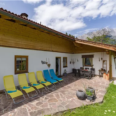 Eine gemütliche Terrasse mit Liegestühlen und einem Essbereich. Im Hintergrund sind die Berge zu sehen und der Himmel ist klar.