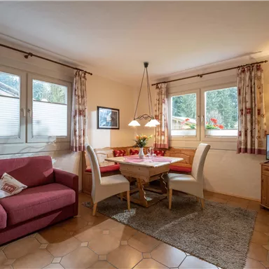 Ein einladendes Wohnzimmer mit einem roten Sofa und einem Holztisch. Große Fenster sorgen für viel Tageslicht und eine gemütliche Atmosphäre.