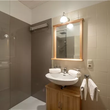 Ein modernes Badezimmer mit einer Dusche und einem Waschbecken. Auf dem Holzschrank liegen Handtücher bereit.