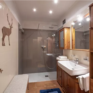 Ein modernes Badezimmer mit Holzregalen und einer großen Dusche. Es gibt einen Waschbecken mit Spiegel und schöne Dekorationen.