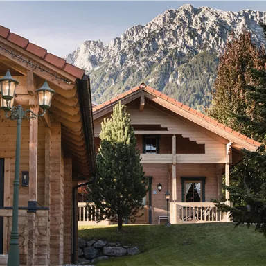 Schöne Holzhütten in einer malerischen Landschaft mit Bergen im Hintergrund. Umgeben von Bäumen und gepflegtem Gras.