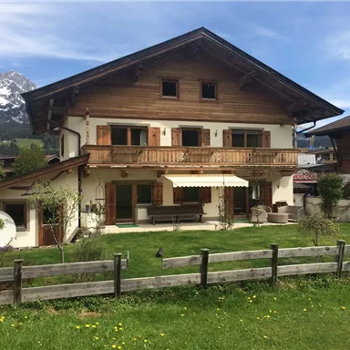 A beautiful wooden house with a balcony and garden. The mountains can be seen in the background.