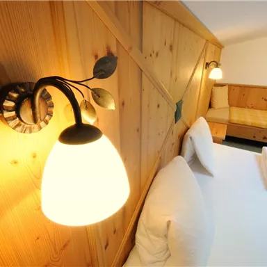 Ein gemütliches Schlafzimmer mit Holzverkleidung und sanfter Beleuchtung. Das Zimmer verfügt über ein großes Bett und eine kleine Couch.