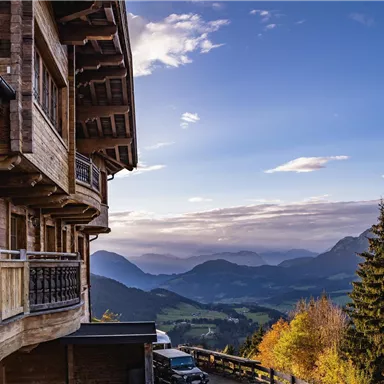 Ein traditionelles Holzhaus mit Blick auf eine malerische Berglandschaft. Der Himmel ist klar und die Natur zeigt herbstliche Farben.