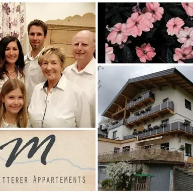 A family stands together and smiles in casual clothing. In the background, the holiday apartments "Haus Mitterer" with balconies and beautiful flowers can be seen.