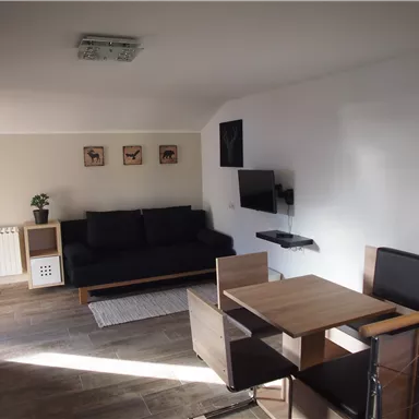 Eine moderne Wohnzimmer mit einem schwarzen Sofa und einem Essbereich aus Holz. An der Wand hängen Bilder, und es gibt einen Fernseher.
