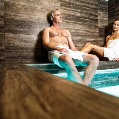 A man and a woman are sitting relaxed in a modern steam bath. They are wearing towels and enjoying the atmosphere.