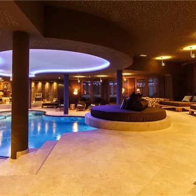 A modern wellness area with a pool and cozy lounge chairs. The soft lighting creates a relaxing atmosphere.