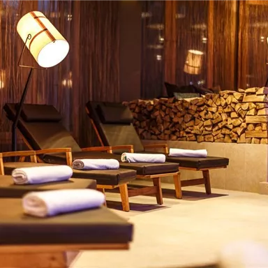 An elegant wellness area with comfortable loungers and relaxing lighting. In the background, there is a stack of wood that creates a cozy atmosphere.