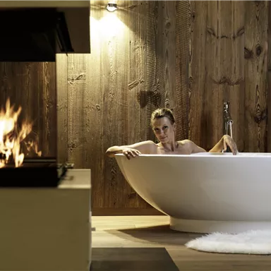 A relaxing bathroom with a modern bathtub and a cozy fireplace. Soft light and wood paneling create a tranquil atmosphere.