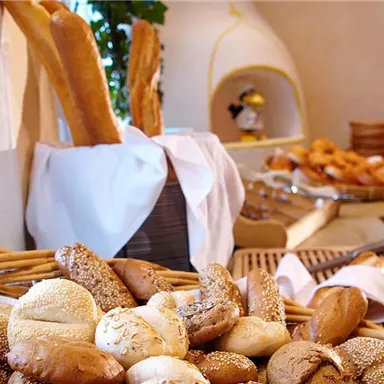 A rich selection of fresh bread and rolls at an inviting buffet. In the background, additional baked goods are visible.