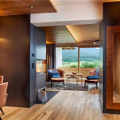 A modern-designed living space with hardwood floors and large windows. Cozy seating creates an inviting atmosphere with a view of the greenery.