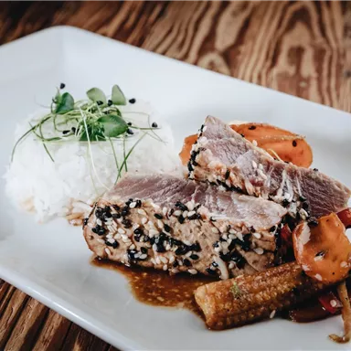 Ein köstliches Gericht mit mariniertem Fisch, Reis und buntem Gemüse. Die Präsentation ist ansprechend auf einem weißen Teller angerichtet.