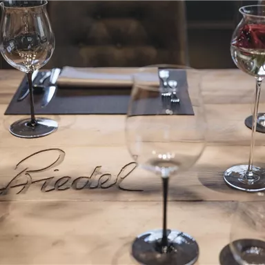 Ein elegant gedeckter Tisch mit Weingläsern und einem Holzuntergrund. Auf dem Tisch steht der Name "Briedel".