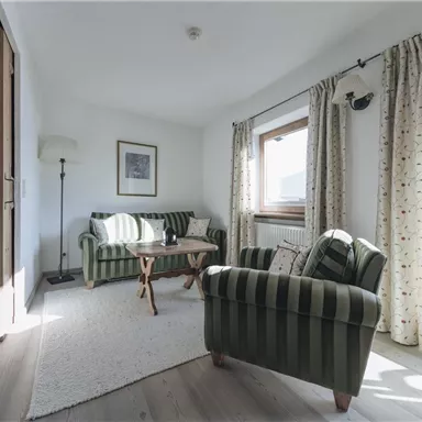 Ein gemütliches Wohnzimmer mit zwei gestreiften Sofas und einem Holzkaffee-Tisch. Große Fenster lassen viel Tageslicht herein und der Raum hat einen einladenden Touch.