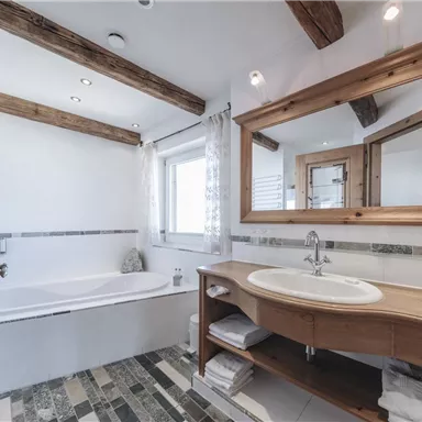 Ein modernes Badezimmer mit einem eleganten Waschtisch und großen Spiegeln. Die Holzbalken verleihen dem Raum eine gemütliche Atmosphäre.