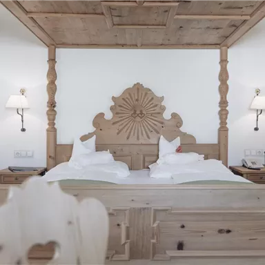Ein elegantes Schlafzimmer mit einem großen, holzgeschnitzten Bett und zwei Nachttischen. Die Wände sind hell und die Beleuchtung ist sanft.
