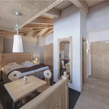 Ein gemütliches Zimmer mit Holzdekor und viel natürlichem Licht. Es gibt einen Tisch, Stühle und ein großes, bequemes Bett.