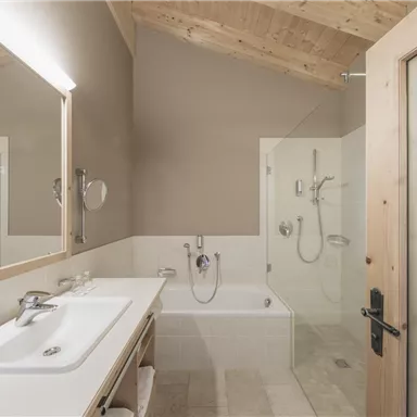 Ein modernes Badezimmer mit Holzwänden und einem großen Spiegel. Es gibt eine Dusche und eine Badewanne, die minimalistisch und stilvoll gestaltet sind.