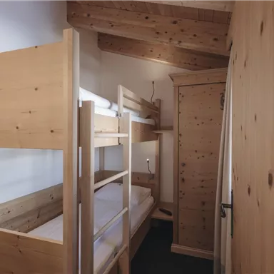 Ein gemütlicher Raum mit einem Etagenbett aus Holz und einem Kleiderschrank. Die Wände sind hell und der Boden ist dunkel, was eine angenehme Atmosphäre schafft.