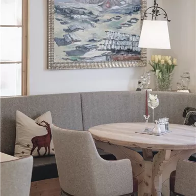 Ein gemütlicher Essbereich mit einer runden Holztisch und gepolsterten Stühlen. An der Wand hängt ein Gemälde von einer Landschaft.