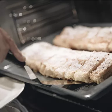 Ein Teller mit frischem Gebäck wird aus dem Ofen genommen. Das Gebäck ist mit Puderzucker bestreut und sieht lecker aus.