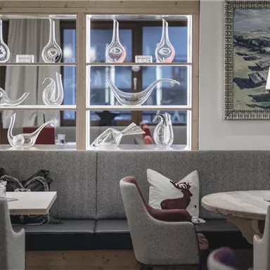 Ein elegantes Restaurant mit gemütlicher Sitzgelegenheit und einem modernen, stilvollen Dekor. Im Hintergrund sind kunstvolle Glasobjekte zu sehen.
