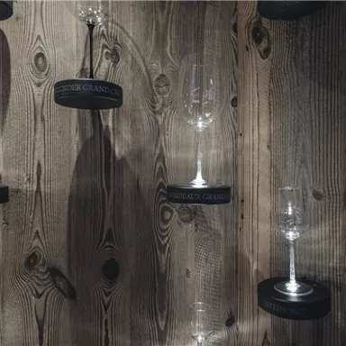 Eine Holzwand mit hängenden Weingläsern in verschiedenen Größen. Die Gläser sind mit schwarzen Beschriftungen versehen.