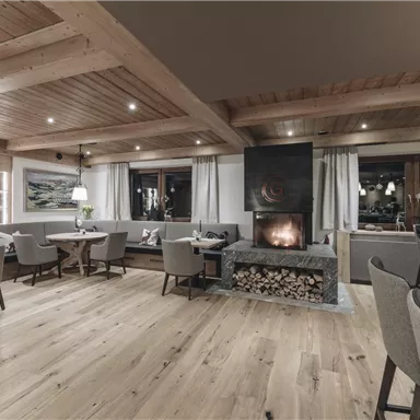 Ein gemütlicher Raum mit Holzböden und Decken. In der Mitte befindet sich ein Kamin, umgeben von bequemen Sitzplätzen.