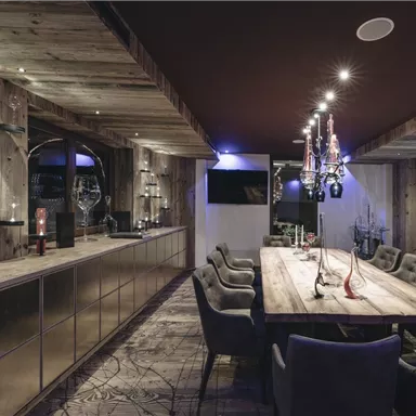 Ein eleganter Speiseraum mit einem langen Holz-Esstisch und bequemen Stühlen. Die Wände sind aus Holz, und es gibt eine stilvolle Beleuchtung.