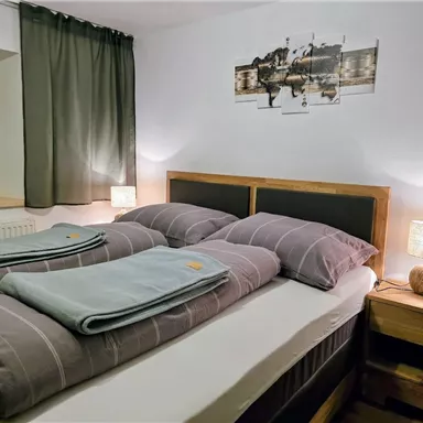 A cozy bedroom with two beds and soft, gray bedspreads. Gentle lighting creates a relaxed atmosphere.