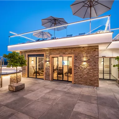 A modern house with a spacious terrace area and sun umbrellas. The pool and stylish architecture give the place an elegant atmosphere.