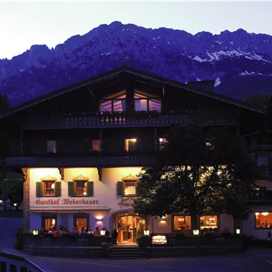 Ein traditionelles Gasthaus in den Bergen, umgeben von majestätischen Gipfeln. Die Beleuchtung des Hauses strahlt eine einladende Atmosphäre aus.