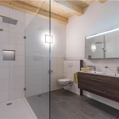 Ein modernes Badezimmer mit einer Dusche und einem eleganten Waschbecken. Die Wände sind hell gefliest, und Holzdetails verleihen Gemütlichkeit.