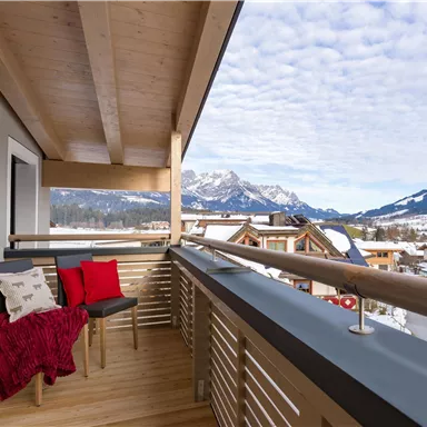 Ein schöner Balkon mit einem Blick auf die Berge. Es gibt einen Stuhl mit roten Kissen und eine warme Decke.