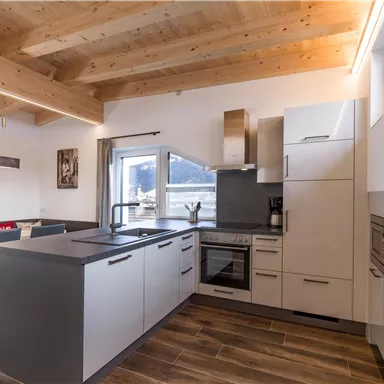 Moderne Küche mit Holzdecken und großen Fenstern. Helle Farben und minimalistische Möbel schaffen eine einladende Atmosphäre.