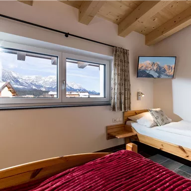Ein gemütliches Schlafzimmer mit zwei Betten und Blick auf die Berge. Große Fenster lassen viel Licht herein und bieten eine schöne Aussicht.